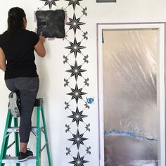 a woman is painting a wall with black and white stars on it, while another person stands on a steplader in front of the door