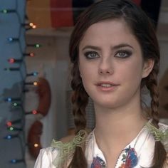 a woman with braids and blue eyes looks at the camera while standing in front of a christmas tree