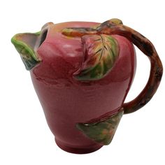 a red ceramic vase with green leaves on the top and bottom, sitting in front of a white background