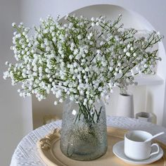 a glass vase filled with white flowers sitting on top of a wooden tray next to a cup and saucer