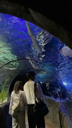 two people standing in front of an aquarium looking at the fish swimming through it's tunnel