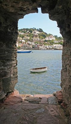 a small boat is in the water through an open stone window that overlooks a town