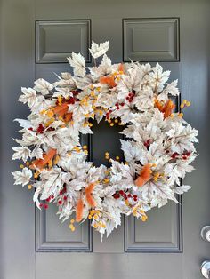 a white wreath with orange and yellow leaves hanging on the front door to welcome guests