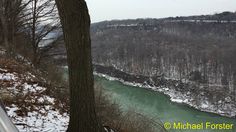 a view of a river in the woods from a hill side viewpoint with snow on the ground and bare trees