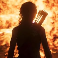 the silhouette of a woman holding two arrows in front of a blazing background with fire