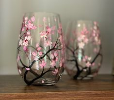 three wine glasses with pink flowers painted on them sitting on a wooden table next to a bottle