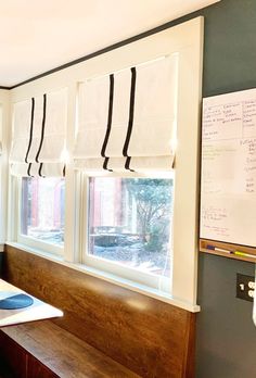 there is a desk with a computer on it in front of two windows that have white and black roman shades