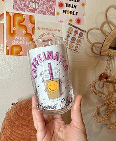 a person holding up a tumbler in front of a wall with stickers on it