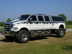 a large white truck parked on top of a grass covered field next to a road