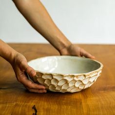 a person holding a white bowl on top of a wooden table