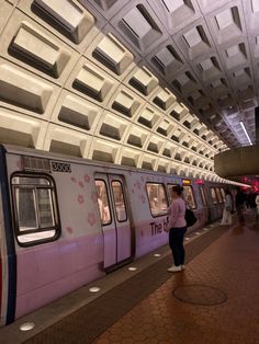 a woman is standing on the platform next to a train that's pulled into the station