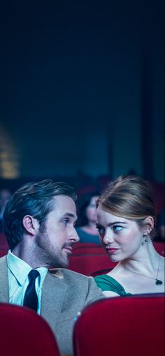 a man and woman sitting next to each other in an auditorium looking at each other