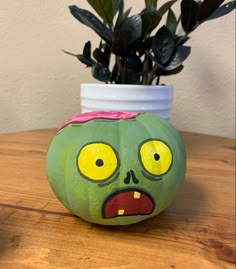 a green painted pumpkin sitting on top of a wooden table next to a potted plant