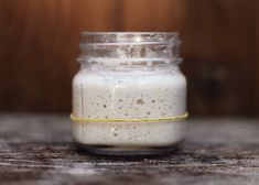 a jar filled with white liquid sitting on top of a wooden table next to a wall