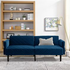 a blue couch sitting in front of a wooden book shelf next to a white rug