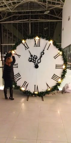 a woman standing in front of a giant clock with lights on it's face