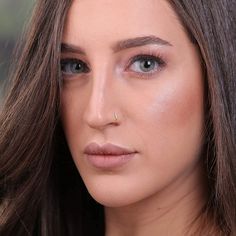 a woman with long brown hair and blue eyes is looking at the camera while wearing a gold nose ring