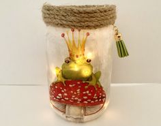 a glass jar with a frog sitting on top of a mushroom and wearing a crown