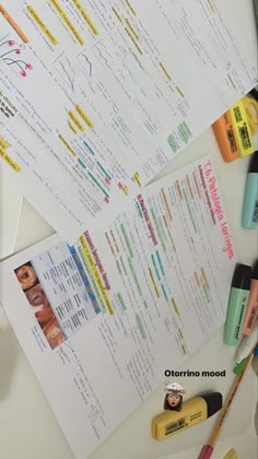 several different types of makeup on top of a white table next to papers and pens