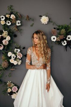 a woman standing in front of flowers wearing a white wedding dress with long sleeves and open back