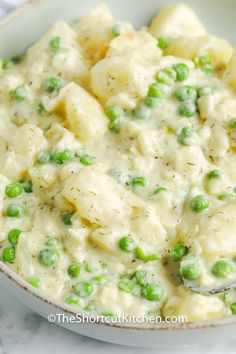 a bowl filled with peas and dumplings on top of a white countertop next to a silver spoon