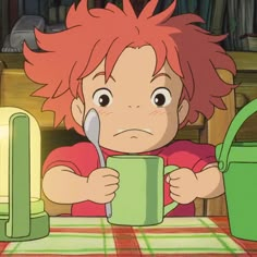 a boy with red hair holding a cup and spoon in front of his face while sitting at a table