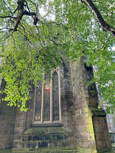 an old stone church with a stained glass window in the center and trees surrounding it