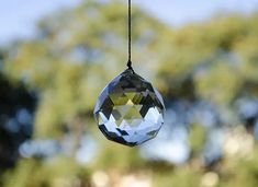 a clear crystal ball hanging from a black string with trees in the backgroud