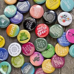 many different colored buttons with words on them sitting on a wooden surface, one has an eyeglass and the other has a smiley face