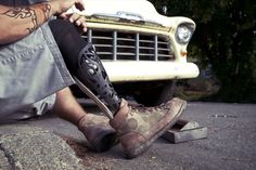 a man sitting on the ground next to a car with his foot propped up against it