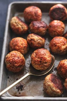 some meatballs are on a baking sheet with a spoon next to them, ready to be eaten