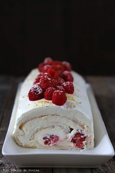 a white plate topped with a roll covered in raspberries and cream frosting