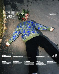 a man laying on the ground with flowers in his hair and wearing a blue shirt