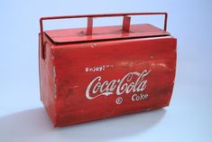 an old coca - cola box is sitting on the floor with its lid open and it's handle still attached