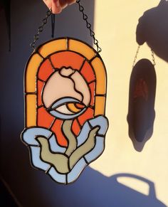 a stained glass window hanging from a chain with a hand holding it up to the viewer