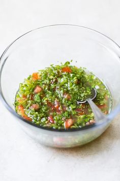 a glass bowl filled with chopped vegetables on top of a white countertop next to a spoon