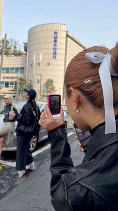 a woman taking a selfie with her cell phone on the street in front of some parked cars