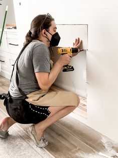 a woman with a driller on her knee working on a wall