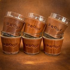 four brown leather cups with the word proof engraved on one side and two glasses in the other