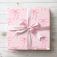 a pink gift box with ribbon and bow on white wooden background, top view from above