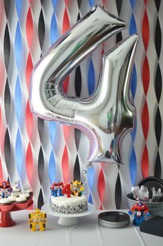 a birthday party with balloons, cake and decorations on the table in front of a striped wall