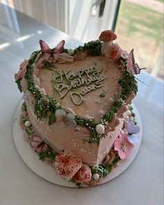 a heart shaped cake with flowers and butterflies on it sitting on a table in front of a window