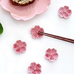 some pink flowers and chopsticks on a white table next to a piece of bread