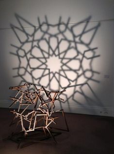 a sculpture made out of sticks in front of a white wall with shadows on it