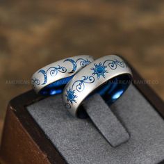 two wedding rings with blue and white designs are sitting in a wooden box on display