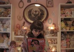 a girl is reading a magazine in front of stuffed animals and other toys on the wall