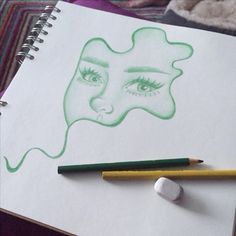 a drawing of a woman's face with green eyes and lips next to two colored pencils