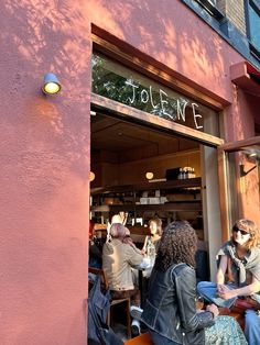 people sitting at tables in front of a store with the door open and writing on it