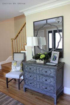 a room with a dresser, mirror and lamp on it's side walk way