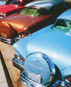 several old cars parked in a row on the side of the road with their hoods down